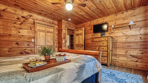 A wooden cabin bedroom with a bed, dresser, television, and a tray with food.