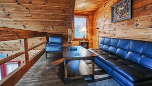 A cabin interior with a wooden ceiling, a sofa, a table, and a window with blinds.