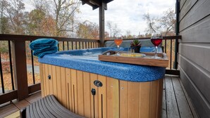 A hot tub with a blue textured surface, a wooden bench, and a tray with a glass of red wine and a glass of orange juice.
