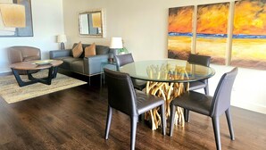 A modern living room with a glass coffee table, leather chairs, a sofa, and a painting of a sunset. - Great Location In Wakiki, Walking Distance To Beach, Shopping, Dining! (Honolulu)