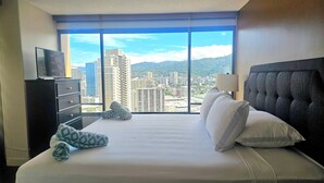 A hotel room with a large bed, a dresser, a TV, and a view of a cityscape. - Great Location In Wakiki, Walking Distance To Beach, Shopping, Dining! (Honolulu)