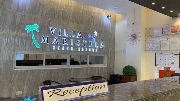 Un comptoir d’accueil avec une enseigne indiquant « Villa Maristela Beach Resort » et un logo représentant un palmier en néon.