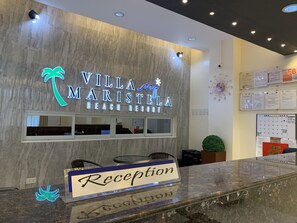 Un comptoir d’accueil avec une enseigne indiquant « Villa Maristela Beach Resort » et un logo représentant un palmier en néon.