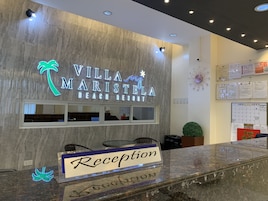 Una recepción con un cartel que dice "Villa Maristela Beach Resort" y un logotipo de palmera de neón.