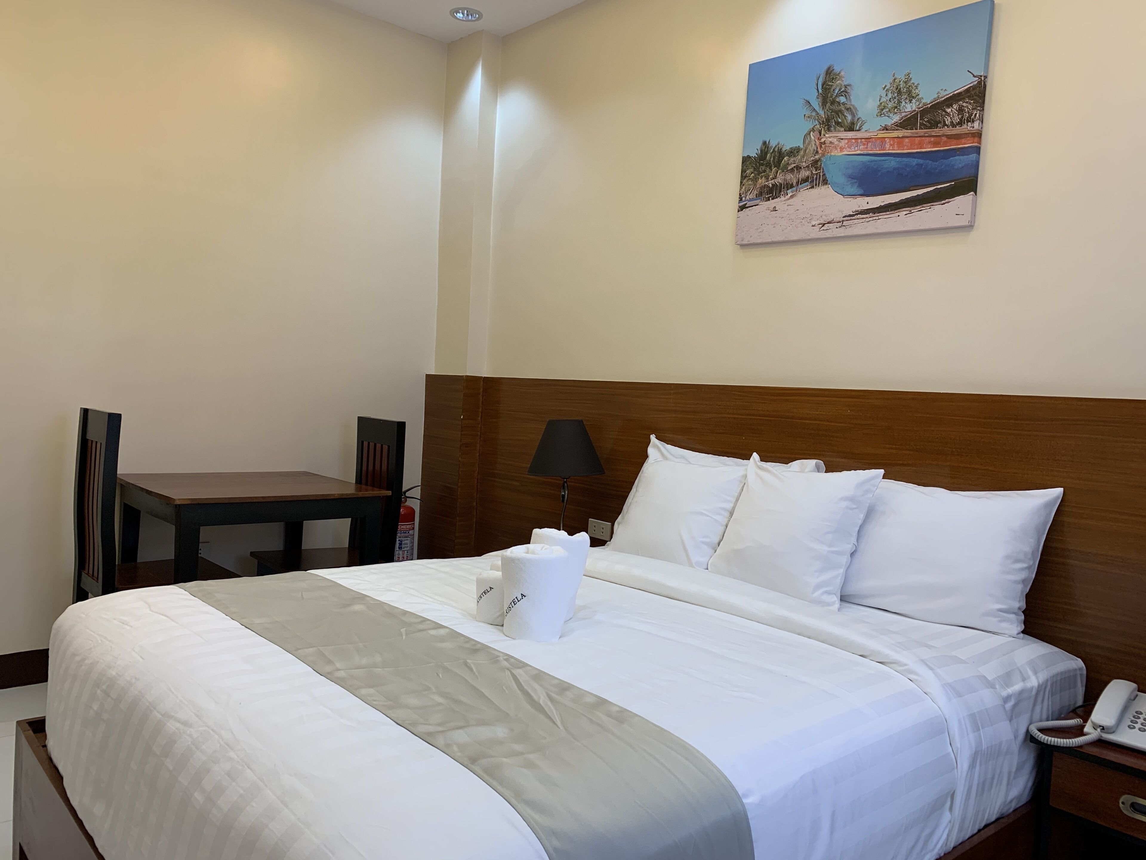 A hotel room with a bed, a desk, a chair, a lamp, and a painting on the wall.