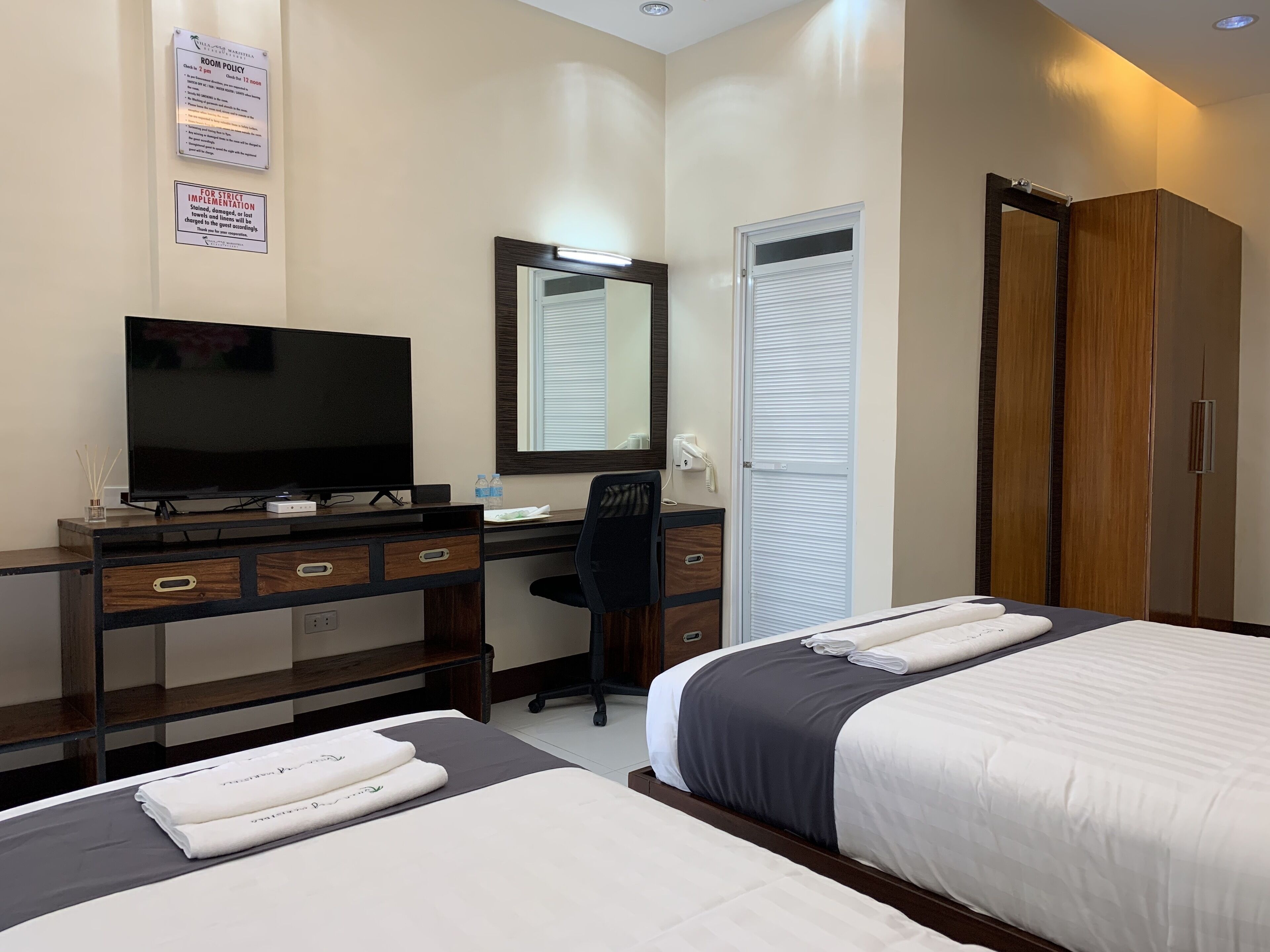 A hotel room with a desk, television, and two beds.