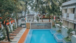 Une piscine entourée de chaises longues et de palmiers, le tout bordé par un bâtiment sur lequel on peut lire l’inscription : « Villa Maristela Beach Resort ».