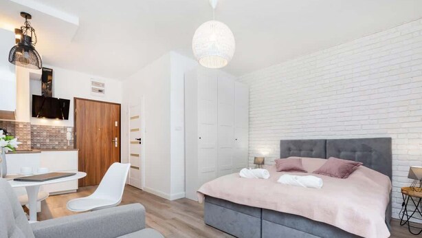 Un dormitorio moderno con una cama grande, un sofá gris, una mesita y un televisor.