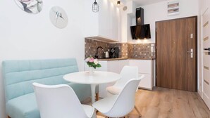 Una cocina moderna con armarios blancos, una puerta de madera y un comedor con un sofá azul claro y sillas blancas.
