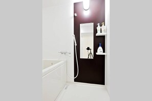 Een badkamer met een bad, een douche en een spiegel. Er staan toiletartikelen op een plankje.