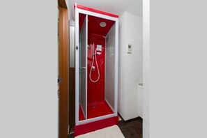 A red and white walk-in shower with a glass door, a white towel on the floor, and a wooden door frame.