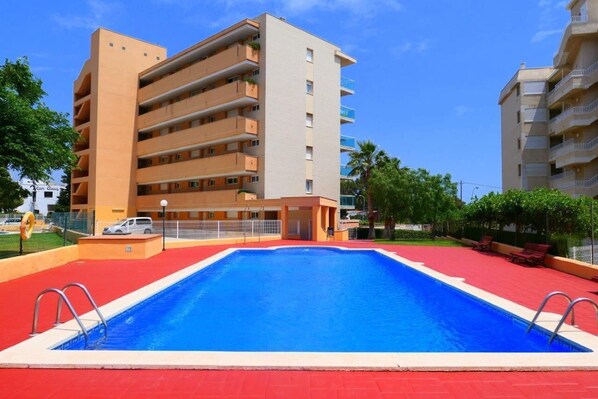 A modern hotel with a swimming pool, multiple balconies, and a red-tiled deck.