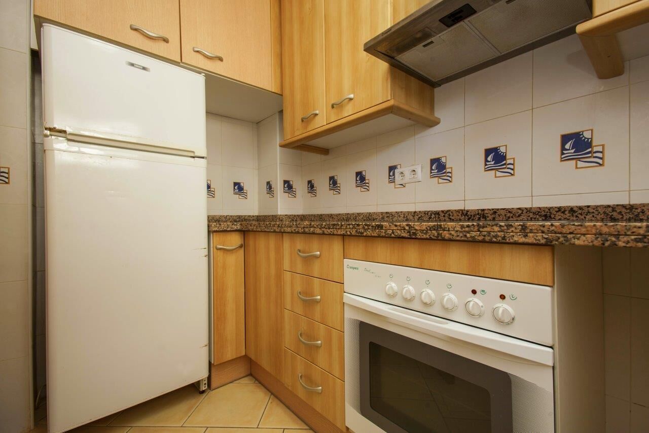 Een keuken met houten kasten, een witte koelkast, een fornuis en een betegelde achterwand met nautische tegels.