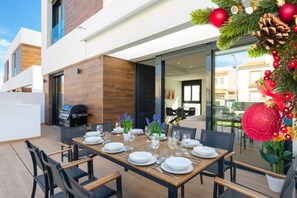 An outdoor dining area with a table set for six, surrounded by chairs, and a grill in the background. - Fidalsa 5 Stars Premium (El Campello)