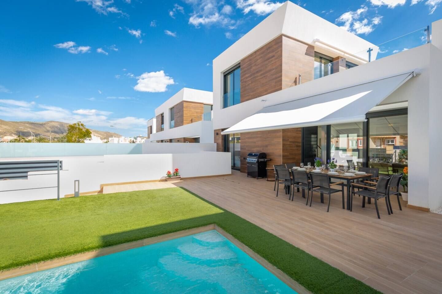 Una casa moderna con piscina, zona de comedor exterior y vistas a las montañas.