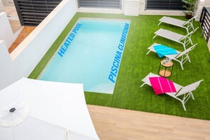 Zona de piscina climatizada con un cartel que indica que es piscina climatizada y un área junto a la piscina con sillones y sombrillas.