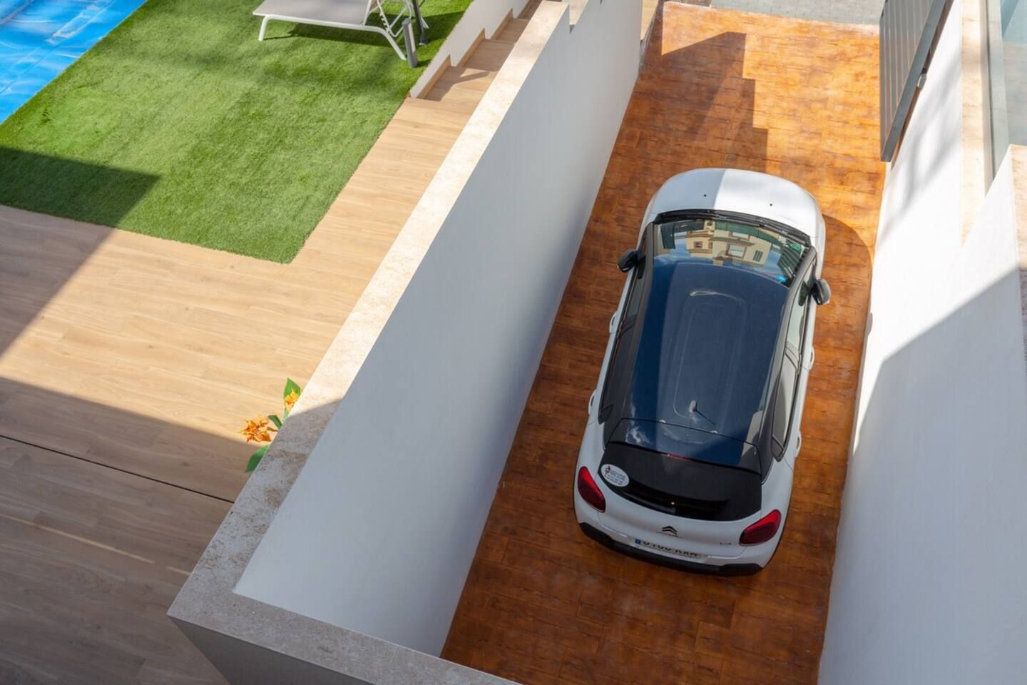 En vit bil parkerad på en smal uppfart med ett trägolv och en vit vägg på ena sidan.