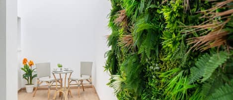 A small room with a white wall, a wooden floor, a white table with two chairs, and a large green vertical garden.