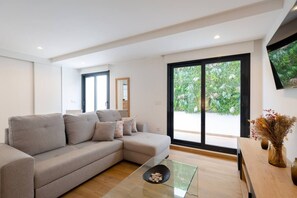 A modern living room with a sectional sofa, a glass coffee table, and a large sliding glass door leading to a garden.