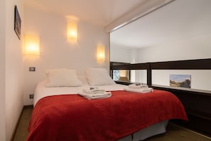 A neatly made bed with white linens and a red blanket, two wall-mounted light fixtures, and a large window with a view of a mountainous landscape. - Grand Roc A211 150m from Slopes, Mont-Blanc View, Parking & WiFi, Argentière (Chamonix), France (Argentière (Chamonix))