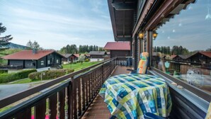 Un balcone con tovaglia a scacchi, ringhiera in legno e vista sulle case circostanti.