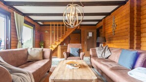 Accogliente interno di una baita in legno con una scala in legno, divani in pelle, un tavolino in legno e un lampadario.