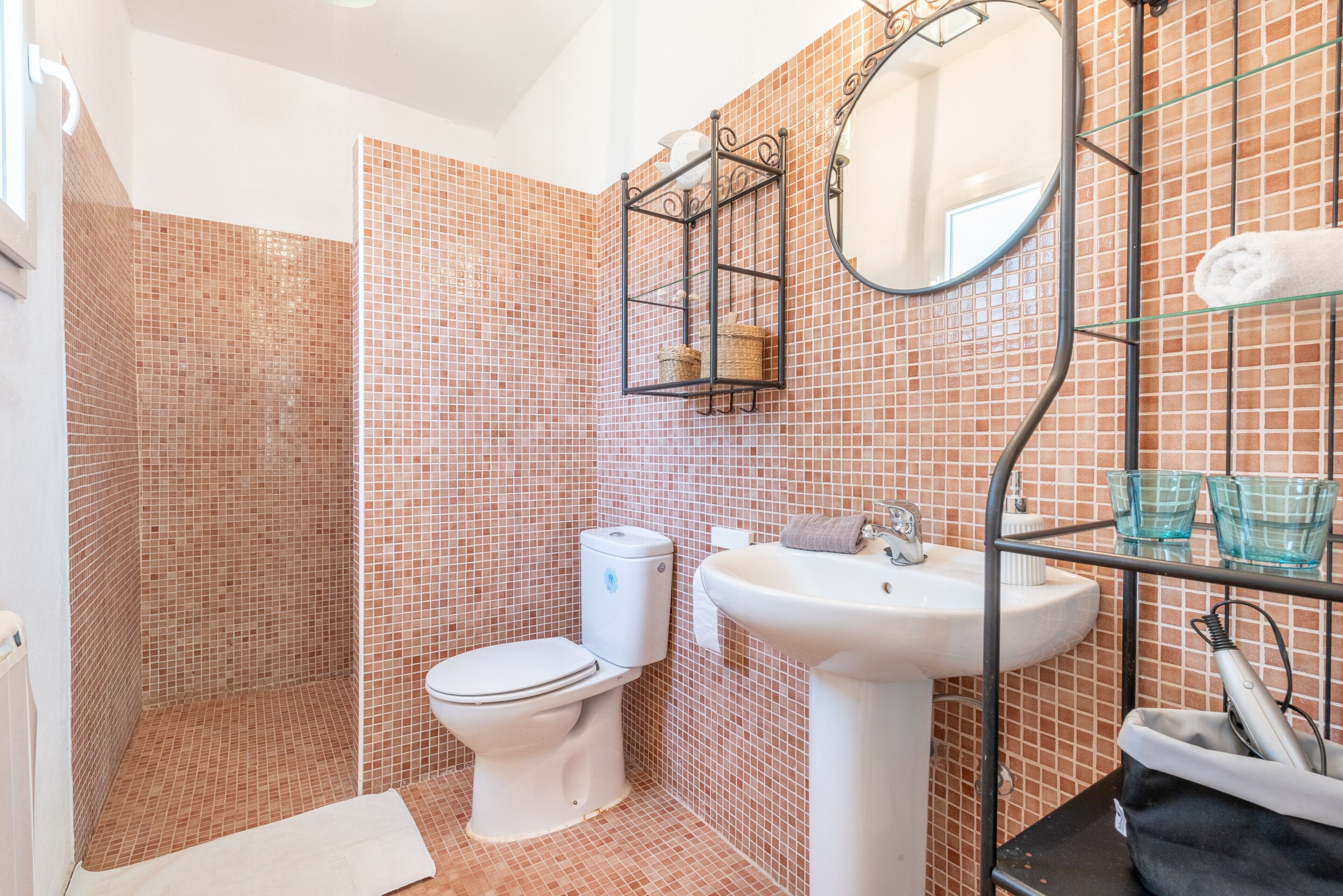 Un baño con ducha empotrada, inodoro, lavamanos, espejo y estante con artículos de aseo.