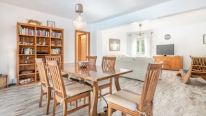 A dining area with a wooden table and chairs, a bookshelf, and a television in the background. - Holiday Home “Polita des Carritxo” with Mountain View, Pool, Garden & Terrace (Es Carritxo)