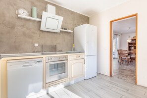 A kitchen with a dishwasher, oven, and refrigerator, wooden cabinets, a microwave, and a dining area with a table and chairs.