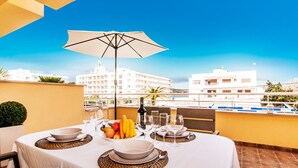 A dining table set with plates, bowls, wine glasses, and a fruit bowl, with a view of buildings in the background. - Apartment “Drac Blanc 1-3” with Sea View, Balcony, Garden & Air Conditioning (Cala Ratjada)