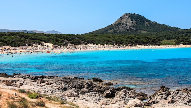 A coastal beach with clear blue waters, rocky shoreline, and a mountain in the background. - Apartment “Drac Blanc 1-3” with Sea View, Balcony, Garden & Air Conditioning (Cala Ratjada)