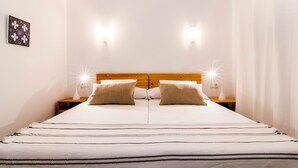 A bed with a wooden headboard, two bedside lamps, and a patterned bedspread. - Apartment “Drac Blanc 1-3” with Sea View, Balcony, Garden & Air Conditioning (Cala Ratjada)