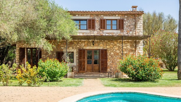 A stone building with a pool, surrounded by greenery and trees.