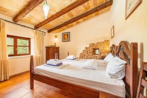 Une chambre avec un lit en bois, un mur en pierre, une fenêtre avec des rideaux et un luminaire suspendu.
