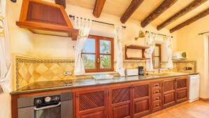 A kitchen with wooden cabinets, a built-in oven, a microwave, and a window with curtains.