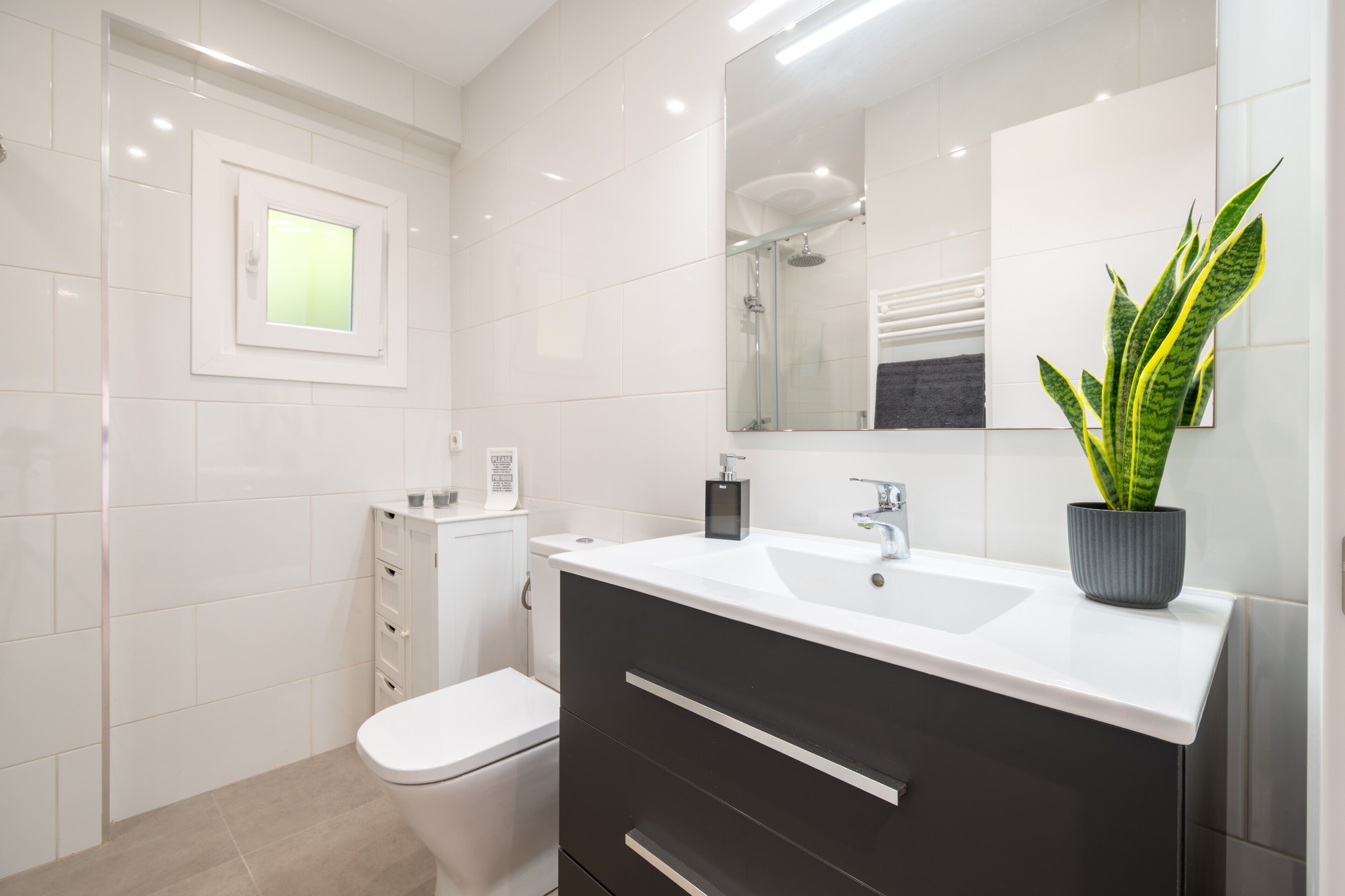 Een moderne badkamer met een wit toilet, een zwarte wastafel met spiegel, en een potplant.