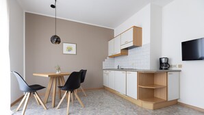 A compact kitchen with a dining area, a coffee machine, and a TV mounted on the wall. - Lovingly Furnished Apartment with Balcony and Stunning City Views in the Residence (Marling)