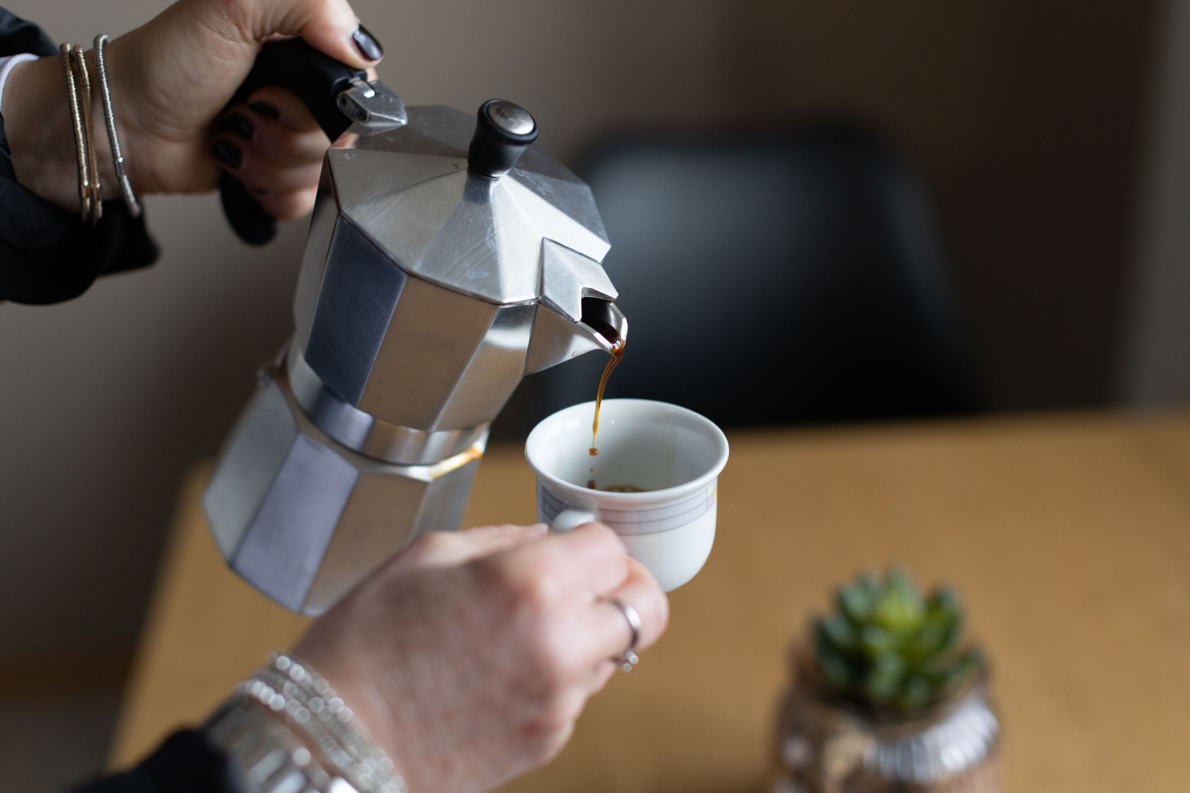 En person häller kaffe från en metallisk espressomaskin i en vit kopp.