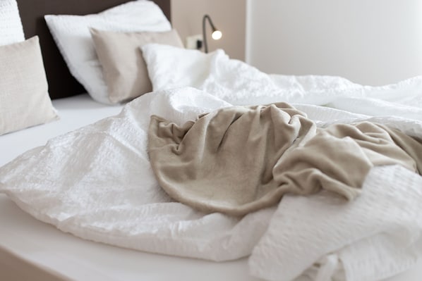 A bed with a white and beige blanket, a pillow, and a bedside lamp.
