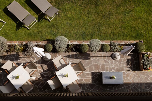An outdoor patio with stone flooring, white tables, and lounge chairs.