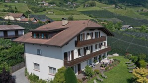 A two-story building with a sloped roof, a balcony, and a well-maintained lawn with outdoor seating. - Lovingly Furnished Apartment with Balcony and Stunning City Views in the Residence (Marling)