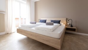 Une chambre moderne avec un lit en bois, deux oreillers, une table de chevet avec une lampe et une vue sur le balcon.