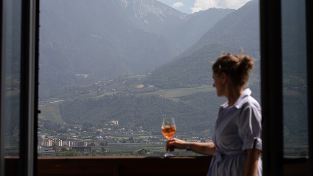 Une personne tenant un verre, avec un paysage montagneux en arrière-plan.