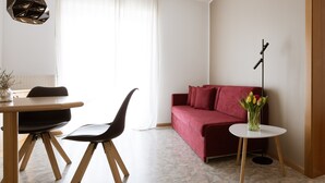 Un salon moderne avec un canapé rouge, une table à manger avec des chaises, un lampadaire et un vase rempli de fleurs.
