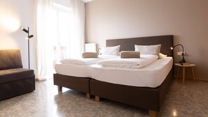 Een moderne hotelkamer met een groot bed, een slaapbank, een nachtkastje en een lamp.