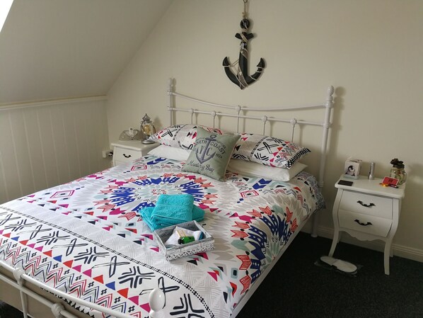 A neatly made bed with patterned bedding, a bedside table with a lamp, and a wall-mounted anchor decoration.