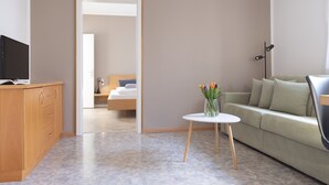 Habitación de hotel con un escritorio de madera, una mesa redonda blanca con un florero y un sofá verde, además de una cama al fondo.