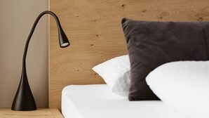 Una cama bien hecha con cabecera de madera, una lámpara de noche y una almohada.