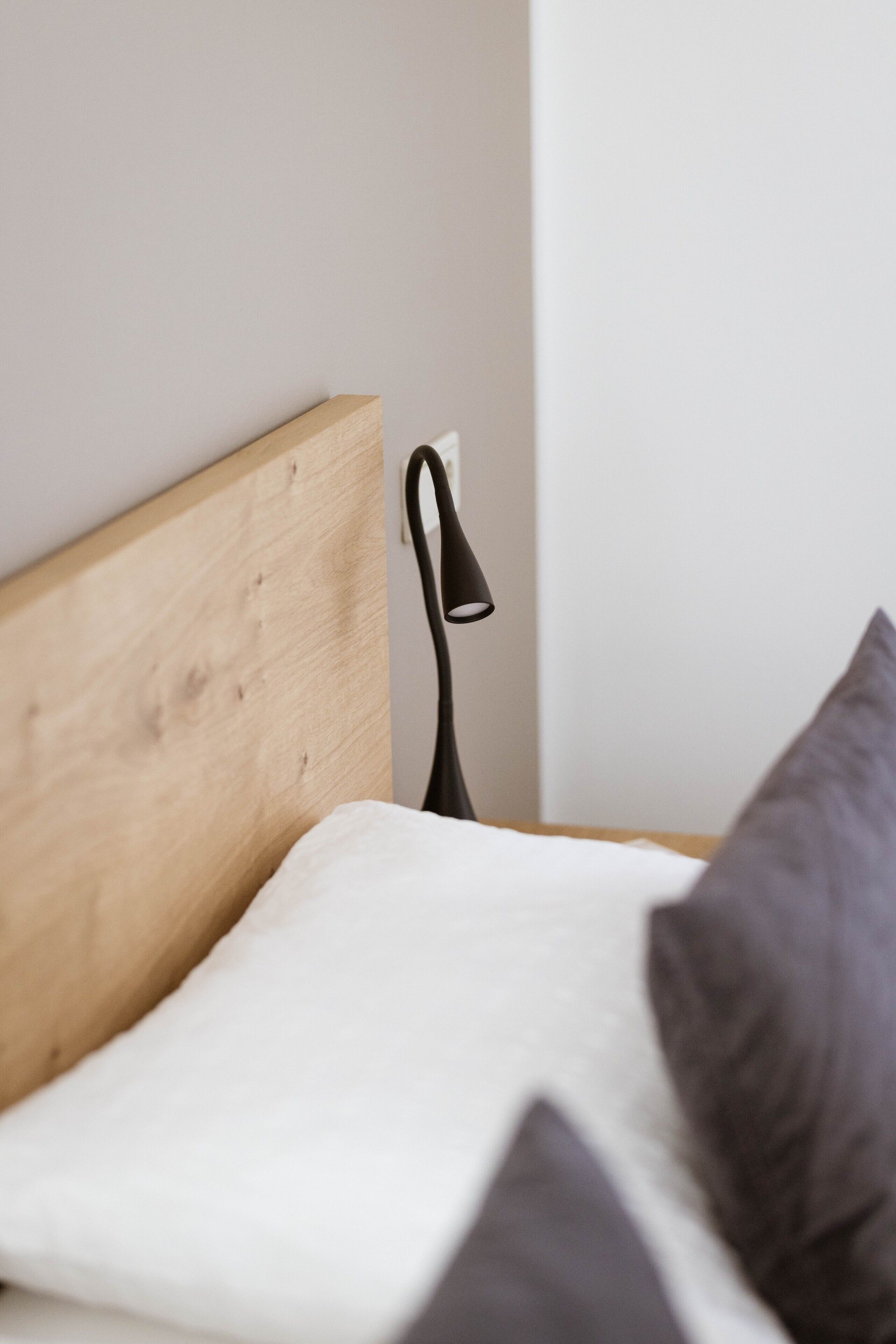 Een bed met een houten hoofdbord, een wit kussen en een zwarte lamp.