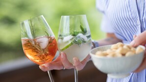 Dos vasos de una bebida con hielo y menta, sostenidos por una persona que tiene un cuenco de aperitivos.